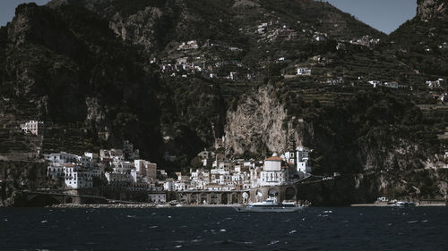Trees and buildings by sea against mountain