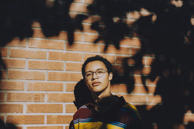 Portrait of young man wearing eyeglasses against brick wall