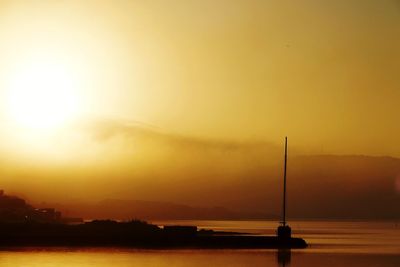 Silhouette sailboat on sea against orange sky