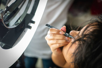 High angle view of young woman applying eyeliner at home