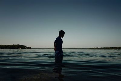 Silhouette boy standing in sea against clear sky