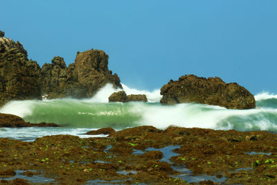 Scenic view of rocks in sea against clear blue sky and wave