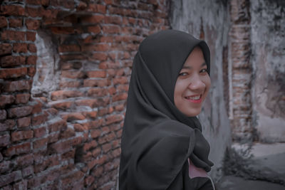 Portrait of smiling woman standing against brick wall