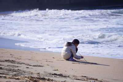 Side view of girl crouching on sand at beach