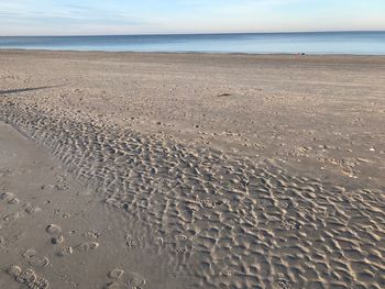 Footprints on sand at beach against sky