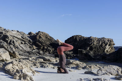 Low section of man sitting on rock against clear blue sky