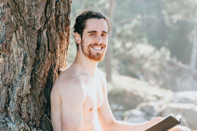 Low angle view of shirtless man sitting on tree trunk