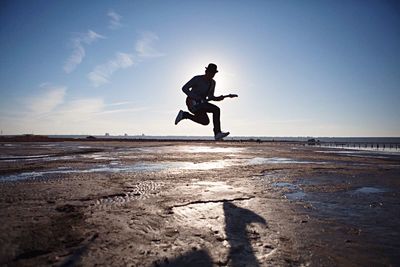 Guitarist jumping over field against sky