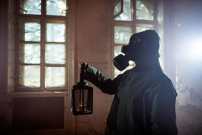 Woman holding oil lamp wearing gas mask standing amidst smoke