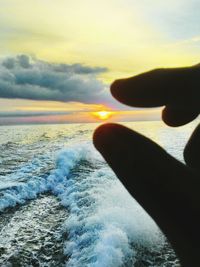 Close-up of hand against sea at sunset