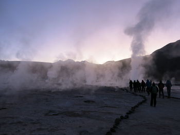 Group of people on smoke emitting from mountain against sky