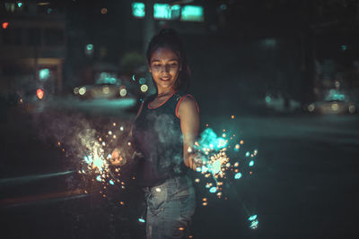 Portrait of smiling young woman standing in city at night