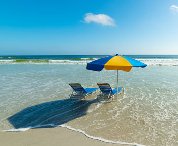 Deck chairs on beach against sky