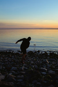 Man standing on rock at beach against sky during sunset