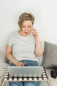 Portrait of young woman using calculator while sitting against white background