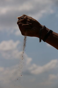 Low angle view of hand holding leaf against sky