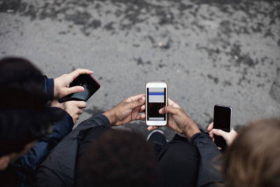 High angle view of male friends using social media while sitting on street