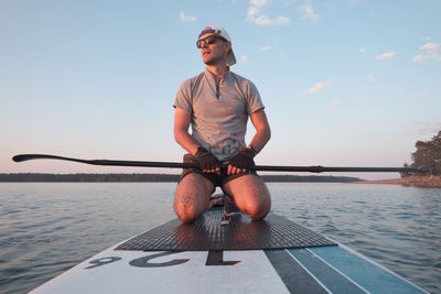 The surfer is resting on the paddleboard. he looks away