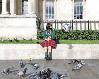 Full length of young woman sitting on wall in city