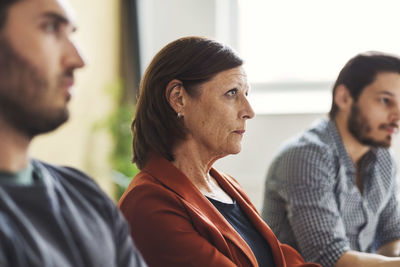 Mature businesswoman with colleagues listening to presentation in meeting room