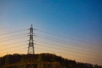 Low angle view of electricity pylons on field against clear sky