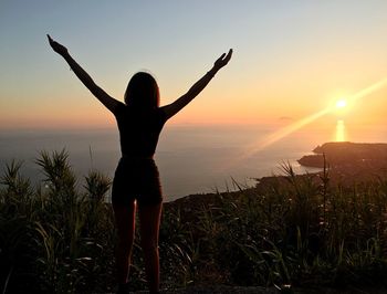 Rear view of woman standing on field against sky during sunset