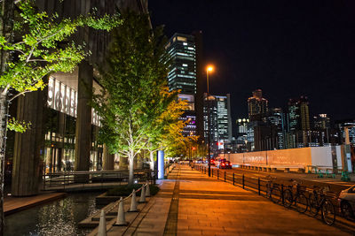 Illuminated street amidst buildings against sky at night