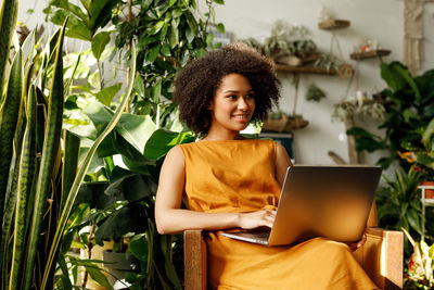 Teenage girl using laptop while sitting against plants