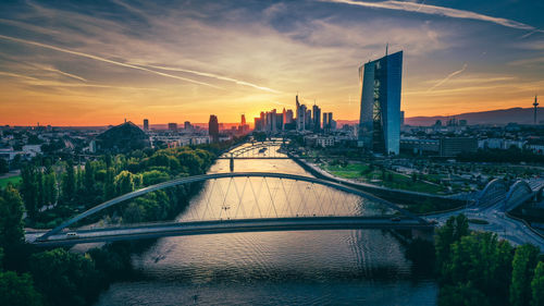 Bridge over river amidst buildings against sky during sunset