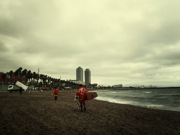 People on beach against cloudy sky