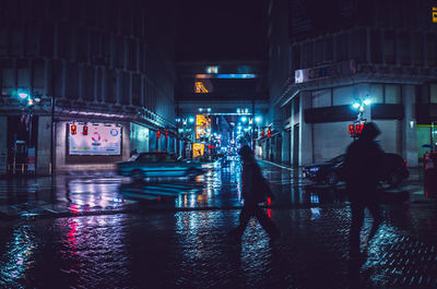 Silhouette people walking on wet street in illuminated city