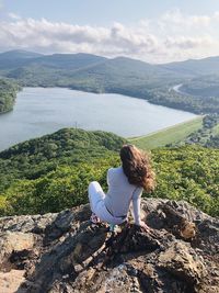 Rear view of woman crouching on cliff against lake