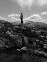 Distant view of woman standing on rock formation against sky