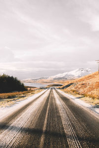 Country road amidst landscape against sky