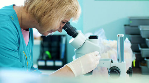 Portrait of lab worker, biochemist in white gloves, studying, examines something with microscope