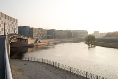 Bridge over river by buildings against clear sky