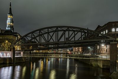 Arch bridge over river against sky in illuminated city at night