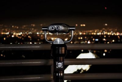 Coin-operated binoculars at observation point against cityscape at night