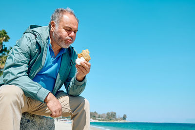 Bearded mature man at spring seaside eating hot palatable panzarotto 