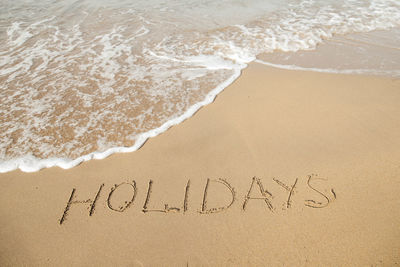 Holidays lettering on the beach with wave and clear blue sea.