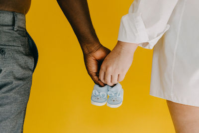 Midsection of couple holding baby booties against yellow background