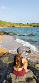 Rear view of woman on rock at beach against sky