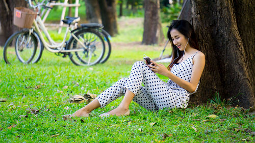 Smiling young woman listening music on headphones while sitting at park