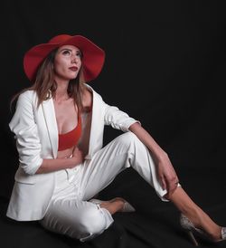 Beautiful woman wearing hat looking away while sitting against backdrop