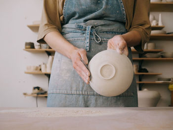 Unrecognizable woman ceramist peeling a clay plate holding sponge. 