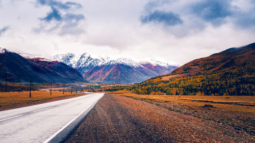 Road leading towards snowcapped mountains against sky