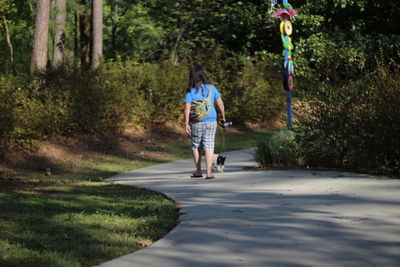 Rear view full length of woman walking with dog on road