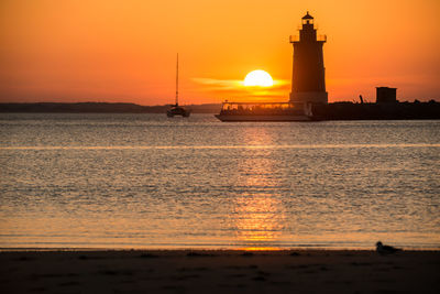 Lighthouse by sea against sky during sunset