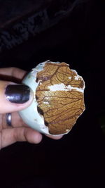 Close-up of hand holding ice cream cone against black background