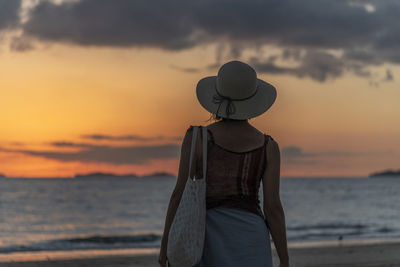 Woman wearing hat on beach against sky during sunset